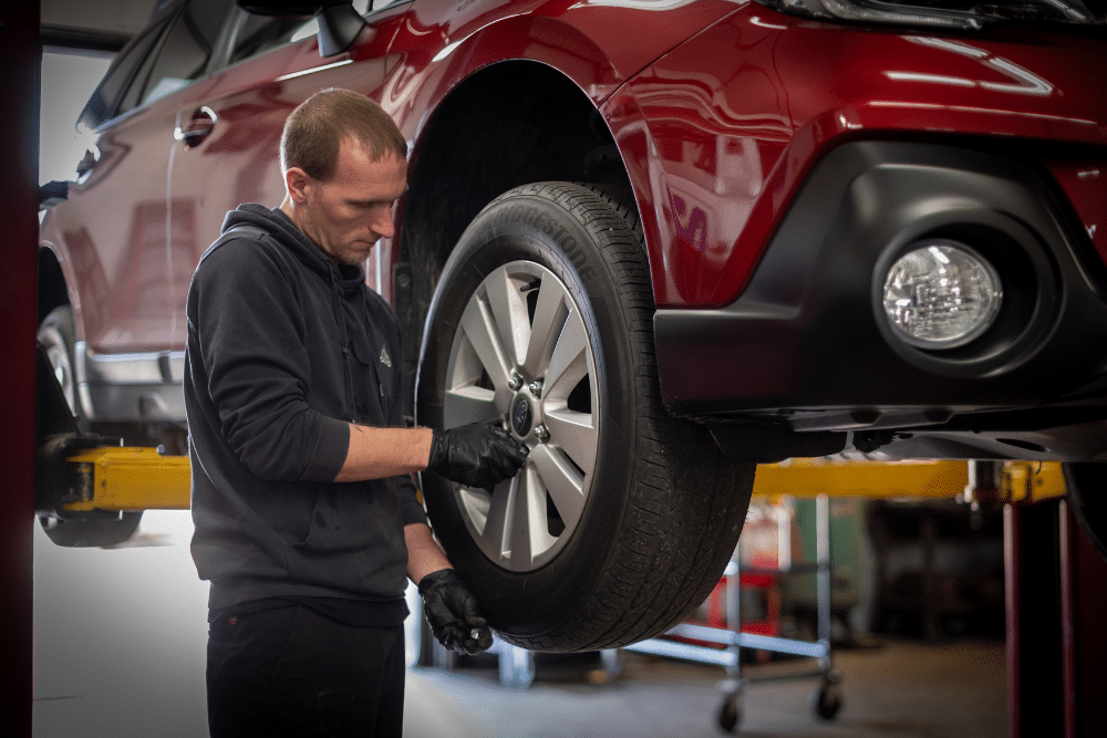 Japanese auto repair, auto repair in Racine, WI at Durand Automotive. A mechanic inspecting a wheel on a red Subaru car lifted on a hydraulic jack.