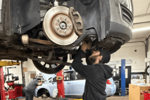 Car check, auto repair in Racine, WI at Durand Automotive. Image of a technician inspecting the suspension and brake components of a vehicle raised on a lift.